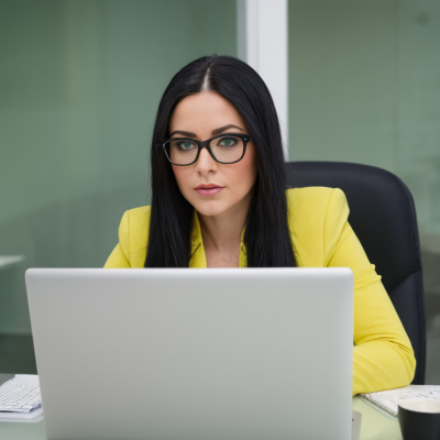Frau mit Brille arbeitet am Laptop in einem modernen Büro.