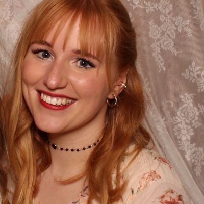 Lächelnde Frau mit rotem Lippenstift vor Spitzenhintergrund.