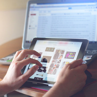 Person nutzt ein Tablet vor einem Laptop.