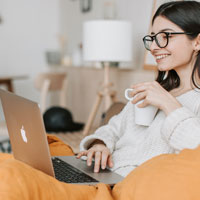 Frau arbeitet lächelnd an einem Laptop und hält eine Tasse.